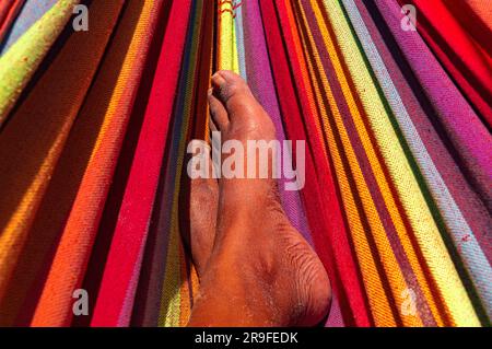 Une vue rapprochée, mettant l'accent sur les pieds d'une personne de couleur reposant tranquillement dans un hamac vibrant et accrocheur. Banque D'Images