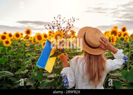 Vue arrière de la femme tenant des drapeaux ukrainiens et bouquet de tournesols champ au coucher du soleil. Paix et liberté Banque D'Images