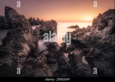 Une plage sur l'océan au lever du soleil, avec un paysage serein de rochers et de vagues doucement lanceuses Banque D'Images