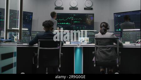 Une équipe de commerçants multiethniques travaille sur des ordinateurs à plusieurs moniteurs avec des stocks en temps réel affichés. Les employés analysent les graphiques du marché des échanges sur plusieurs grands écrans. Négociation et investissement de crypto-monnaies. Banque D'Images