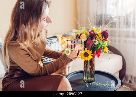 Arrangement de fleurs. Femme fait automne bouquet de fleurs solaires dahlias roses et zinnies dans vase à la maison avec chat. Banque D'Images