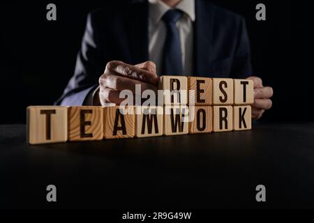 Un homme d'affaires tient entre ses mains un bloc de cube en bois avec des mots sur l'arrière-plan de la table Banque D'Images