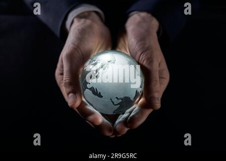 Un homme tient un globe lumineux dans ses mains. gros plan sur un arrière-plan noir Banque D'Images