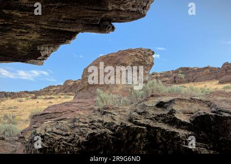 Vue d'une petite grotte aux grandes rochers et brosse sèche contre un ciel clair et lumineux près de Buhl, Idaho. Banque D'Images