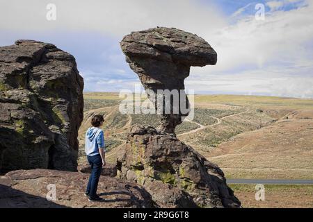 Une jeune femme se tient sur une corniche de roche en regardant le célèbre Balanced Rock près de Buhl, Idaho. Banque D'Images