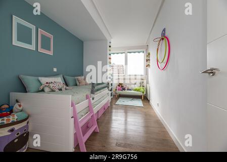 Chambre jeune avec lit en bois blanc avec deux matelas roses, commode et murs peints en deux tons Banque D'Images