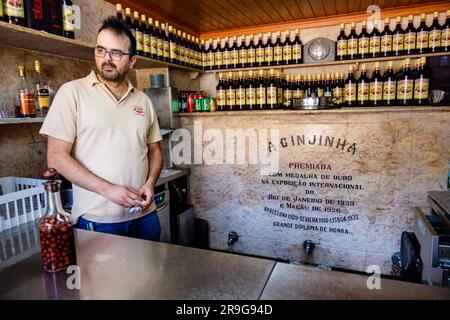 Bouteilles de liqueur de cerise aigre Ginjinha sur étagère, ouvrier à l'intérieur D'Un bar Ginginha, Largo de São Domingos, Praça de São Domingos, Rossio, Lisbonne, Portugal Banque D'Images