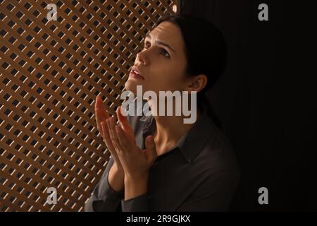 Femme priant à Dieu pendant la confession en cabine Banque D'Images