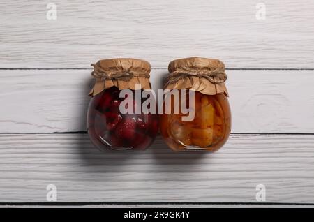 Bocaux avec fruits marinés sur table en bois blanc, plat Banque D'Images