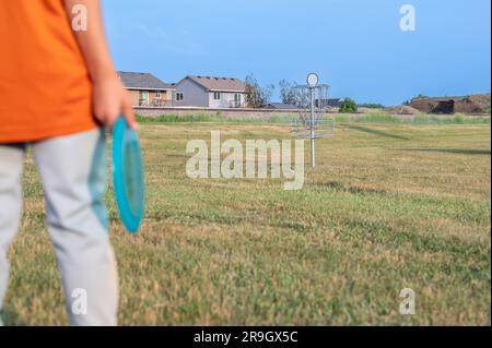 Herbe de fairway à focalisation sélective avec un jeune enfant défoqué tenant un disque de putter et un but de golf au loin. Banque D'Images