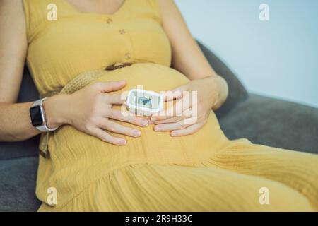 Femme enceinte avec oxymètre de pouls sur le doigt. Médecin mesurant le niveau de saturation en oxygène en visitant la mère expectative avec la maladie de coronavirus à Banque D'Images