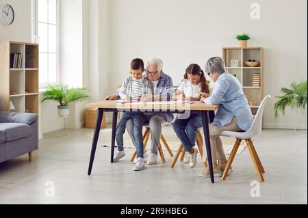 Des grands-parents de couple passent du temps avec des petits-enfants à la maison à dessiner à table. Banque D'Images