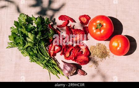 Appétissant tomates séchées et fraîches, diverses épices et herbes se trouvent sur la table de cuisine, lumière du soleil et ombre Banque D'Images