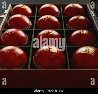 Une collection de balles de cricket rouges imprimées avec les logos dorés des douze pays affiliés à la CPI, disposées dans une boîte d'exposition en bois recouverte de feutre - juin Banque D'Images