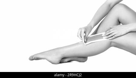 Des jambes bien entretenues après l'épilation, isolées sur fond blanc. Cirage de la jambe de femme avec une bande de cire au spa de beauté. Noir et blanc Banque D'Images