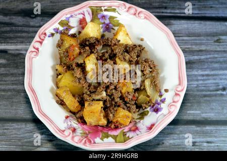 Cuisine égyptienne des cubes de pommes de terre frits, puis cuits avec de la viande de bœuf hachée à l'huile, à l'ail, à l'oignon, aux tomates et au poivre servis dans une assiette isolée sur le bois Banque D'Images