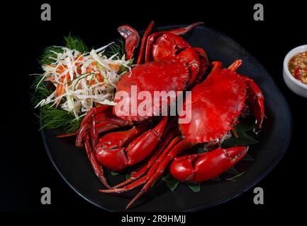 Gros plan de crabes cuits à la vapeur sur une assiette noire servi sauce épicée de style thaï Banque D'Images