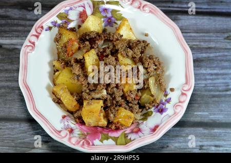 Cuisine égyptienne des cubes de pommes de terre frits, puis cuits avec de la viande de bœuf hachée à l'huile, à l'ail, à l'oignon, aux tomates et au poivre servis dans une assiette isolée sur le bois Banque D'Images