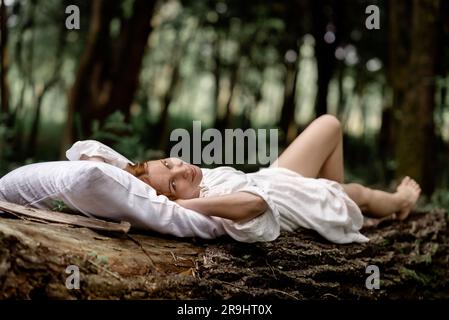 Repos, détente dans la forêt.Une femme repose sur un oreiller sur un arbre entouré d'un feuillage vert. Banque D'Images