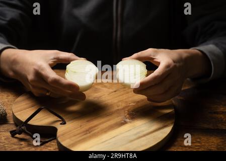 moitiés d'un oignon brut dans les mains d'une femme sur fond de bois. Banque D'Images