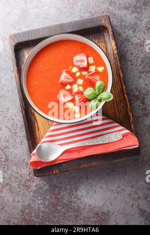 Soupe espagnole de tomates gazpacho avec fraises, concombres et basilic dans un bol sur la table. Vue verticale du dessus Banque D'Images