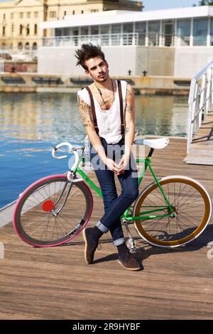 Vélo, mode et jeune homme au bord de la mer dans un groupe punk ou rock lors d'un séjour urbain. Tatouage, confiance et portrait d'un grunge ou d'une edgy sérieux Banque D'Images