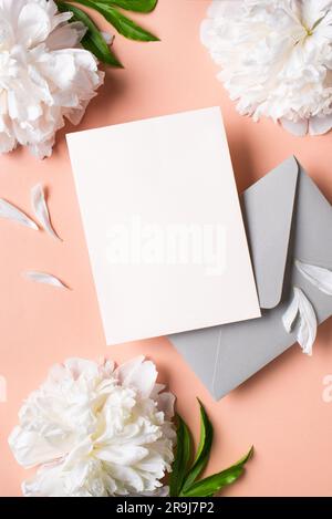 Carte vierge de vœux ou d'invitation, fleurs de pivoine et enveloppe sur fond rose pastel, espace de copie. Maquette créative élégante, mariage romantique ou Hol Banque D'Images