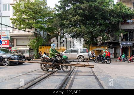 Hanoï, Vietnam-avril 2023 ; vue à angle bas d'une route très fréquentée avec scooter transportant des tuyaux traversant les voies de chemin de fer de la célèbre ligne de chemin de fer à travers ce Banque D'Images