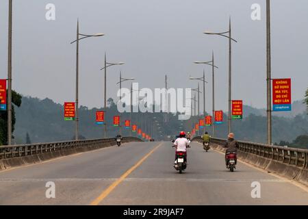 Bac Ha, Vietnam-avril 2023; perspective des conducteurs vue sur la route avec seulement quelques trottinettes sur un pont large et long avec des lampadaires décorés de fla Banque D'Images