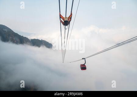 Sa Pa, Vietnam-avril 2023 ; vue à grand angle du téléphérique approchant le sommet de la montagne Fanxipan avec des montagnes de niveau inférieur partiellement couvertes de faible pendre Banque D'Images