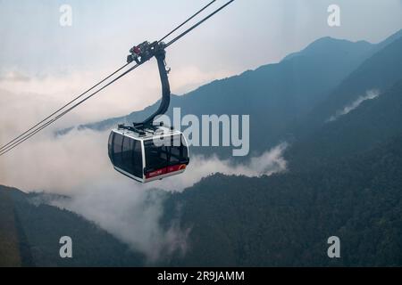 Sa Pa, Vietnam-avril 2023 ; vue à grand angle du téléphérique approchant le sommet de la montagne Fanxipan avec des montagnes de niveau inférieur partiellement couvertes de faible pendre Banque D'Images