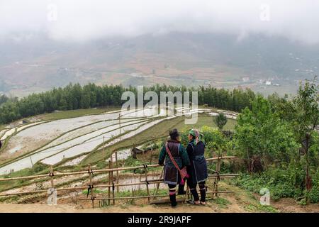 Sa Pa, Vietnam-avril 2023 ; vue en grand angle de deux Hmong indigènes se tenant sur une clôture surplombant les rizières dans la vallée en contrebas Banque D'Images