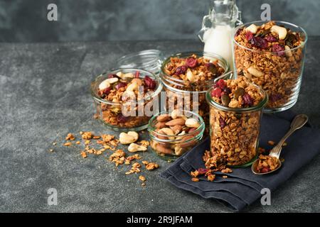 Granola maison dans un pot en verre avec yaourt grec ou lait et noix de cajou, amandes, citrouille avec graines de canneberges séchées sur fond de table gris foncé. Santé Banque D'Images