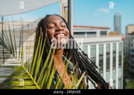 Portrait de jeune africaine américaine joyeuse avec de longs dreadlocks yeux fermés tenant vos cheveux le jour ensoleillé Banque D'Images