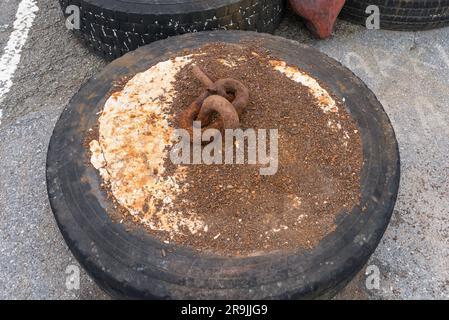 Vieux pneus remplis de béton avec une chaîne rouillée fixée pour maintenir les bouées d'amarrage Banque D'Images