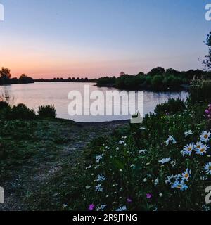 La photo capture un coucher de soleil hypnotisant sur le lac Croxall au Royaume-Uni. Le ciel est éclatant avec des teintes vibrantes d'orange, de rose et de pourpre, moulé Banque D'Images