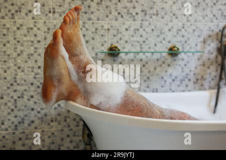 Les pieds pour hommes sont recouverts d'un bain moussant dans une baignoire de luxe avec bonheur et détente Banque D'Images