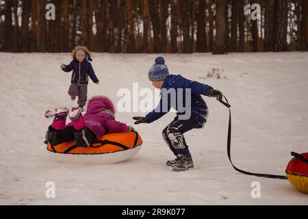 Les enfants montent en hiver à partir d'une glissade de glace sur un tubing multicolore. Bébé souriant et heureux avec tube de neige, glissant sur une pente enneigée. Banque D'Images