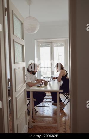 Couple marié indépendants assis à table dans la salle de séjour avec des ordinateurs portables et travaillant à domicile Banque D'Images
