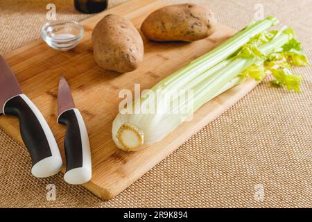 Branche de céleri et pommes de terre en gros plan sur panneau de bois. Légumes crus pour une recette de soupe de céleri gros plan sur la table de cuisine sur fond rustique Banque D'Images