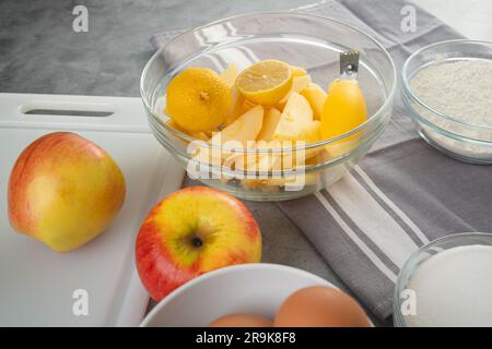 Moule à pâtisserie avec des tranches de pomme, du citron, des œufs, du sucre et de la farine dans des bols en gros plan sur une table de cuisine. Recette de gâteau aux pommes, processus de préparation Banque D'Images