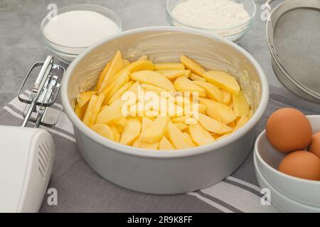 Moule à pâtisserie avec des tranches de pomme, des œufs, du sucre et de la farine dans des bols en gros plan sur une table de cuisine. Recette de gâteau aux pommes, processus de préparation Banque D'Images