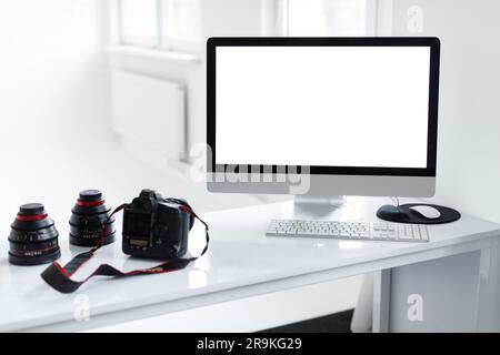 Moniteur d'ordinateur vierge, photocamera et accessoires d'appareil photo sur le lieu de travail du photographe en studio photo léger, maquette Banque D'Images
