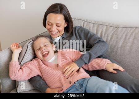 Riant millénaire caucasienne dame hug fille de l'adolescence, ont le plaisir, étant tickled, profiter de temps libre sur le canapé Banque D'Images