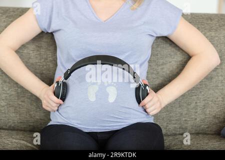 femme enceinte mettant des écouteurs sur le ventre Banque D'Images