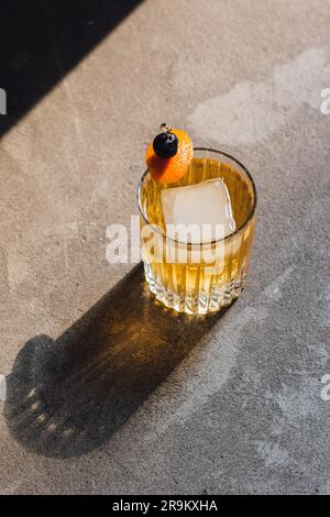 cocktail de whisky avec grande glace en cristal double verre à l'ancienne sur béton au soleil avec garniture orange et cerise Banque D'Images