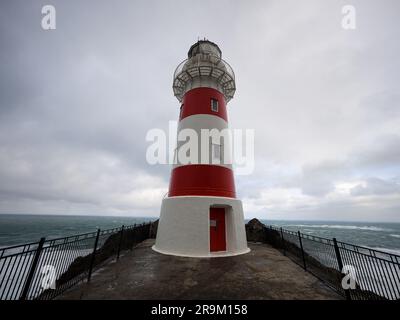 Vue panoramique sur le phare à rayures rouges et blanches perché au sommet d'une colline de falaise au bord de l'océan, Cape Palliser Wellington North Island New Zealan Banque D'Images
