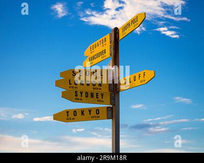 Panneau d'information jaune indiquant les destinations de la ville mondiale et les flèches de direction avec ciel bleu à Cape Reinga North Island Nouvelle-Zélande Banque D'Images