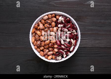 Différents types de haricots secs dans un bol sur une table en bois, vue de dessus Banque D'Images