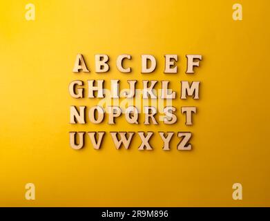 Ensemble de 26 lettres en bois, alphabet entier sur fond jaune, vue de dessus. Banque D'Images